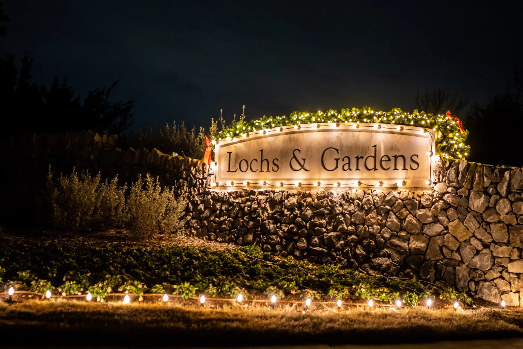 Lochs & Gardens stone monument with warm white stake lighting and holiday greenery
