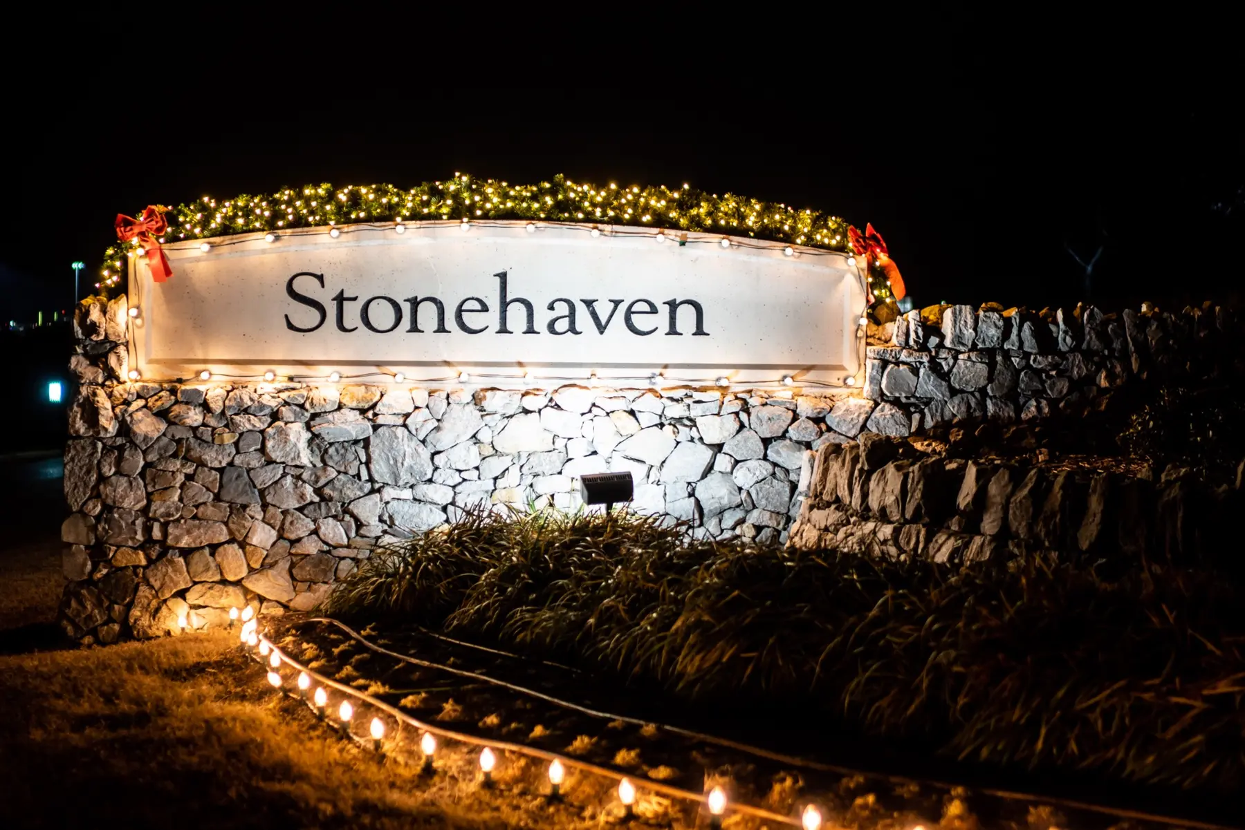 Stonehaven stone monument with warm white stake lighting and holiday greenery