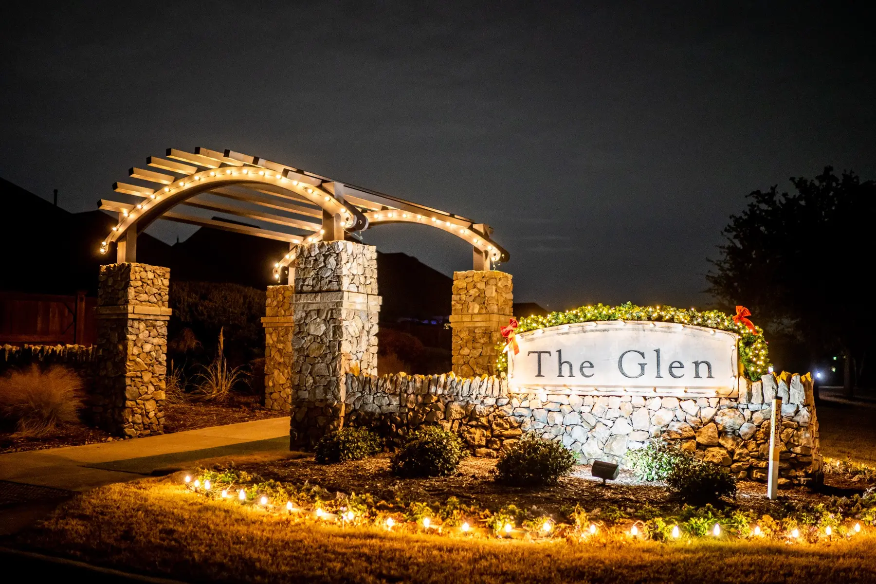 The Glen community entrance with warm white stake lighting and arch accents