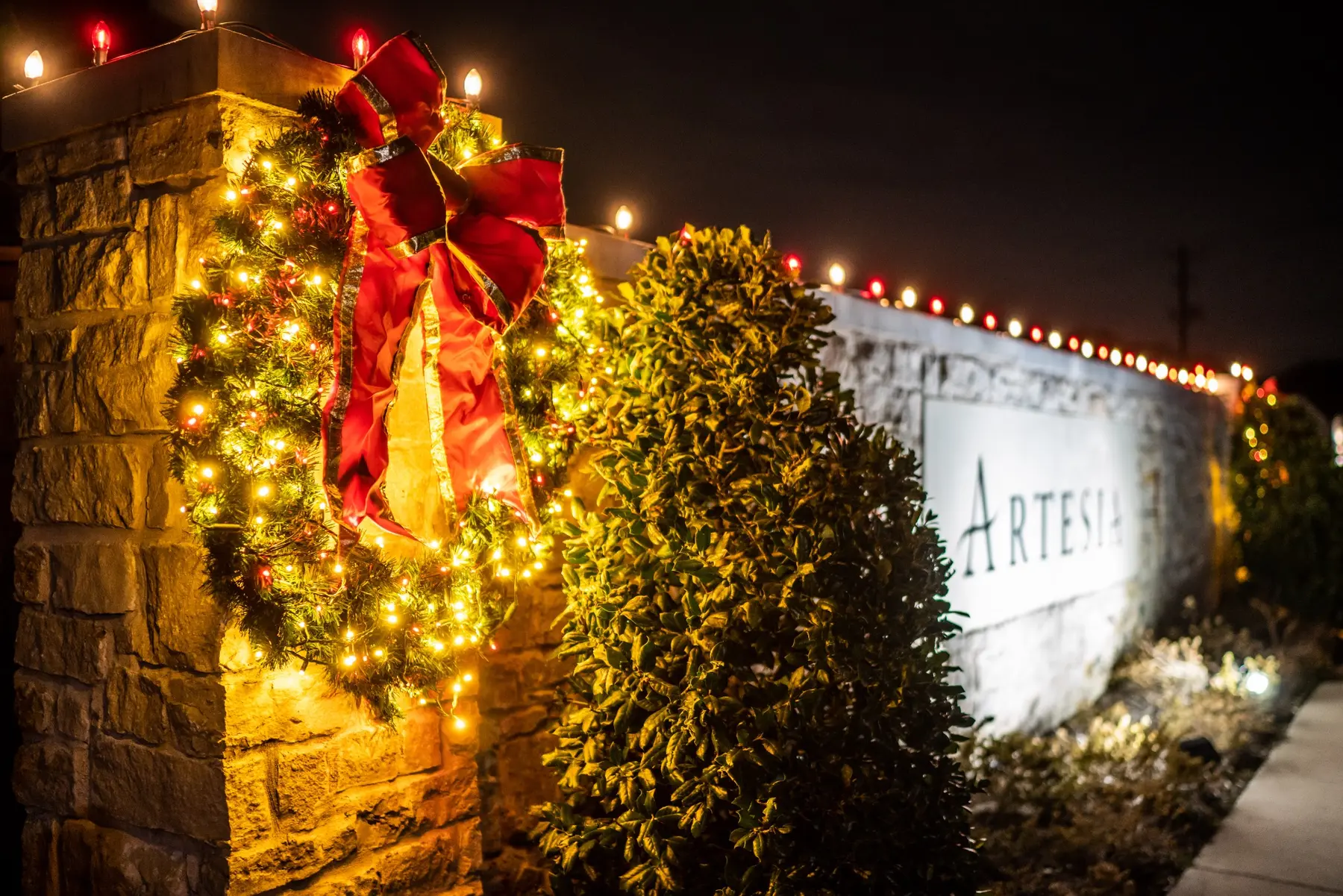 Large lit wreath with a red bow mounted on a stone community monument