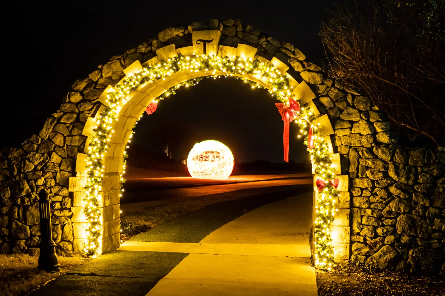 Stone arch wrapped in lit garland with an illuminated ornament visible beyond it