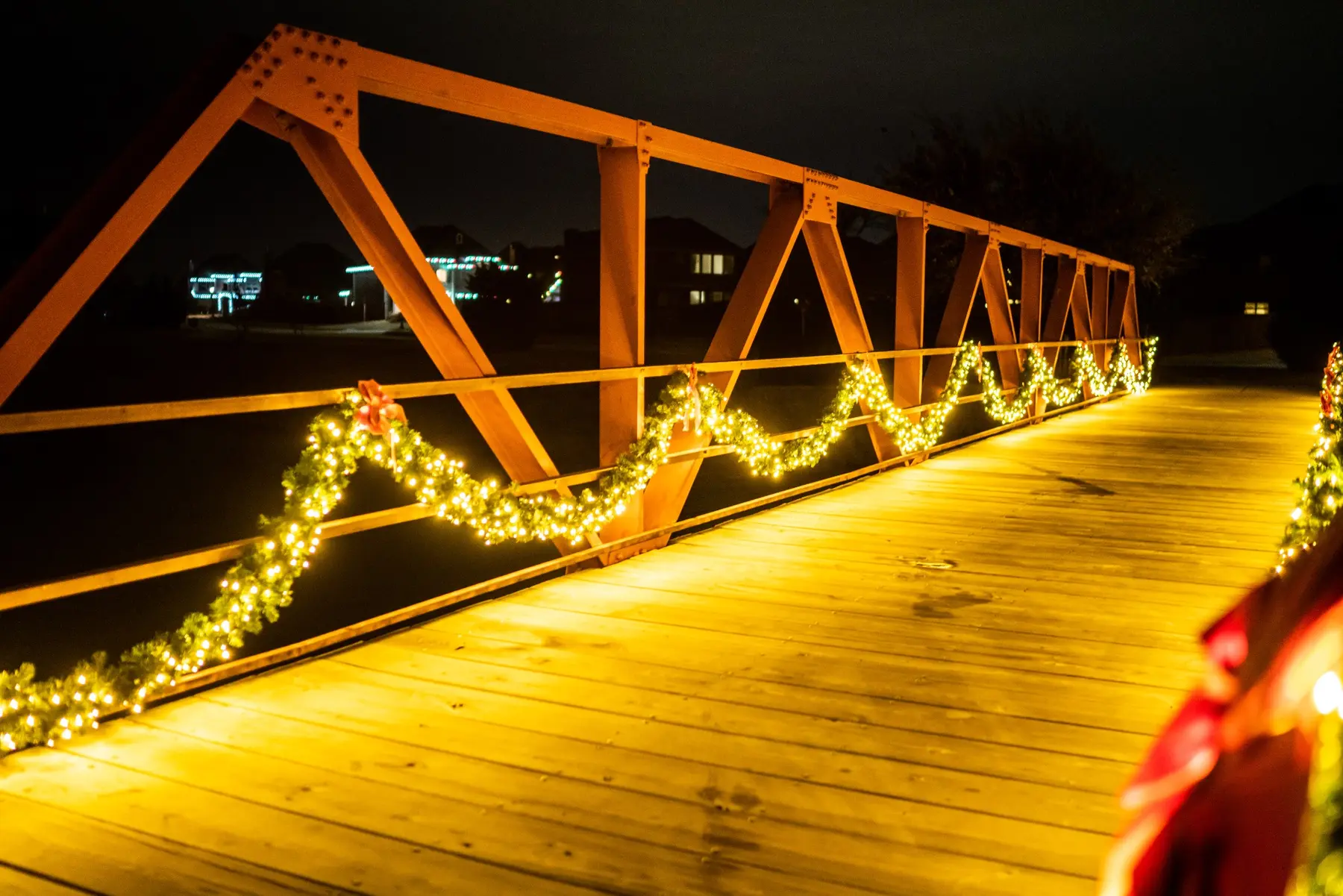 Pedestrian bridge railing draped with lit garland and red bows