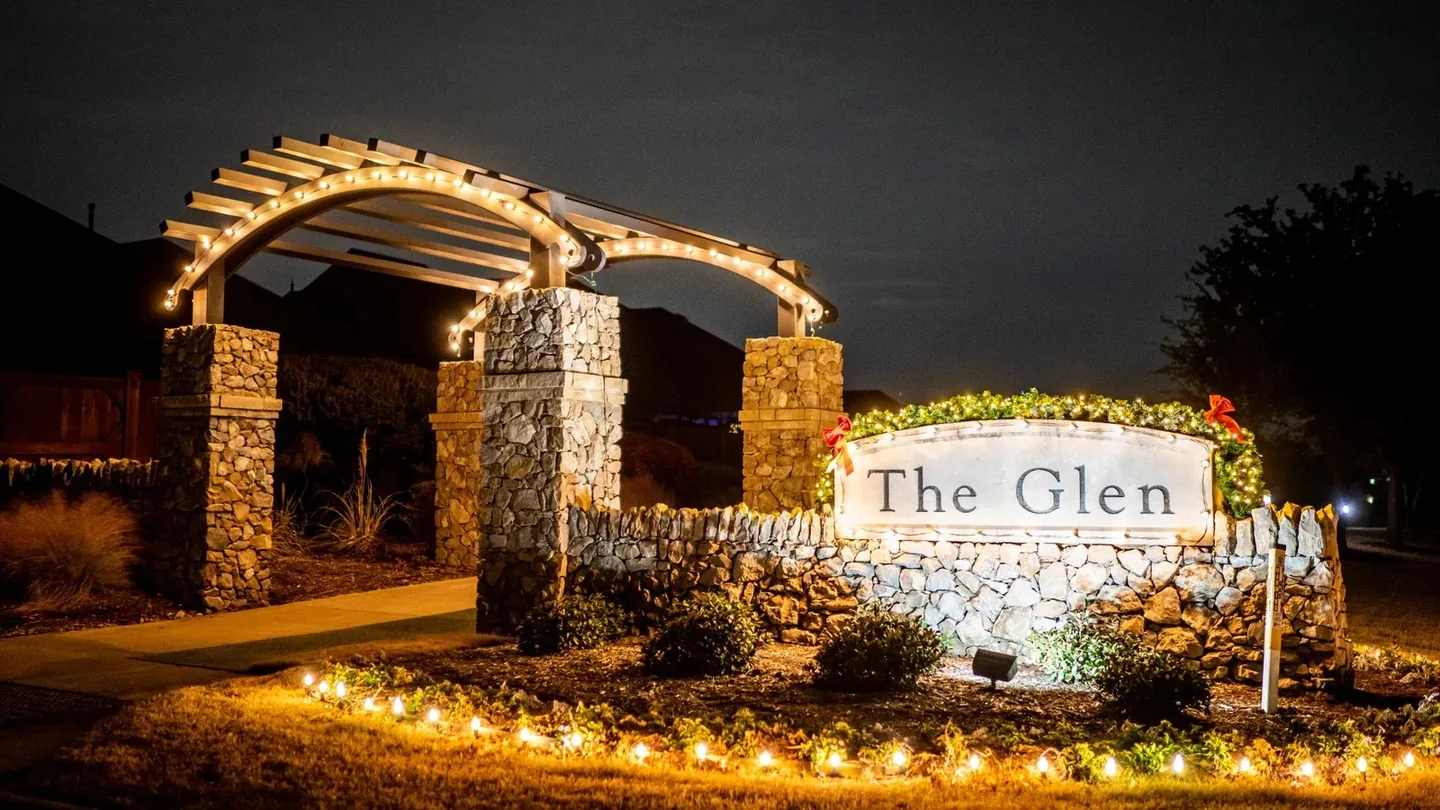 The Glen entrance monument with warm white holiday lighting and landscape accents