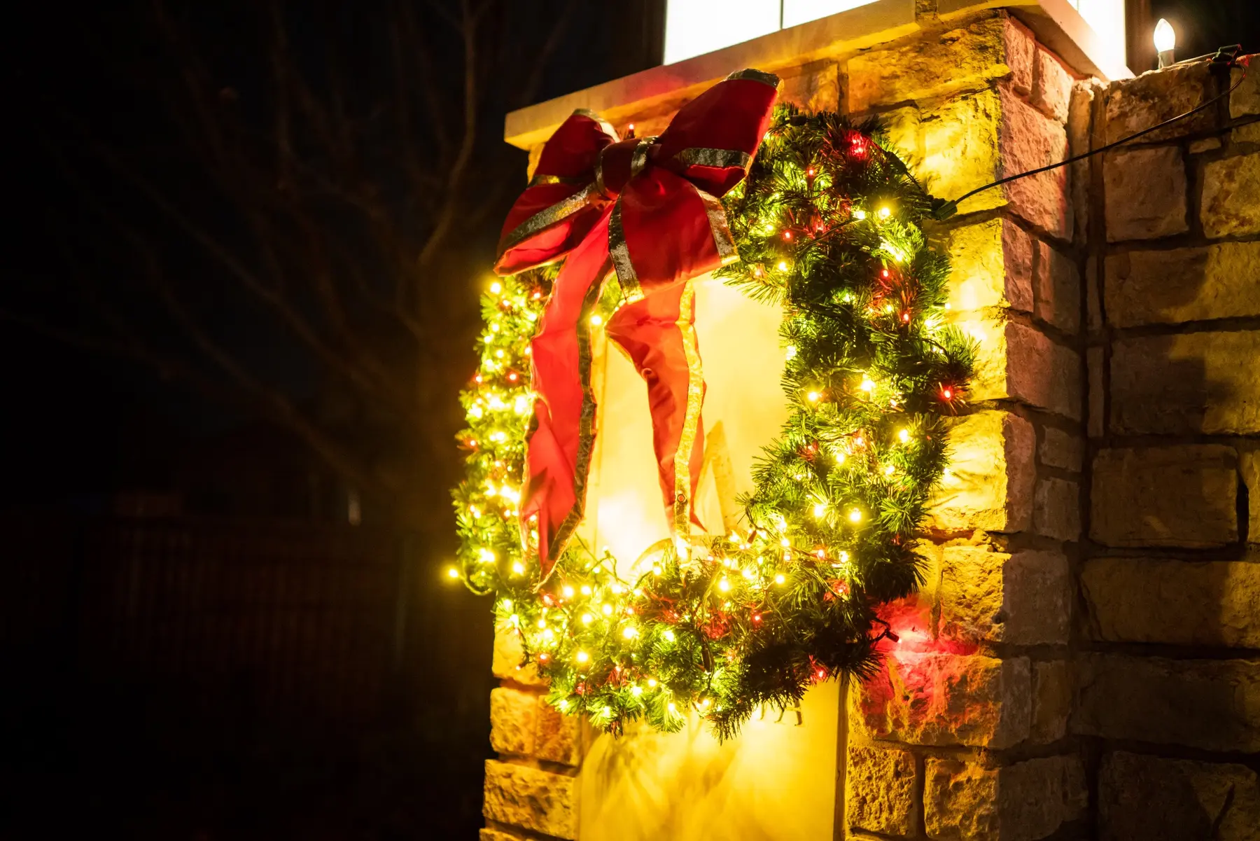 Large lit wreath with a red bow mounted on a stone residential column