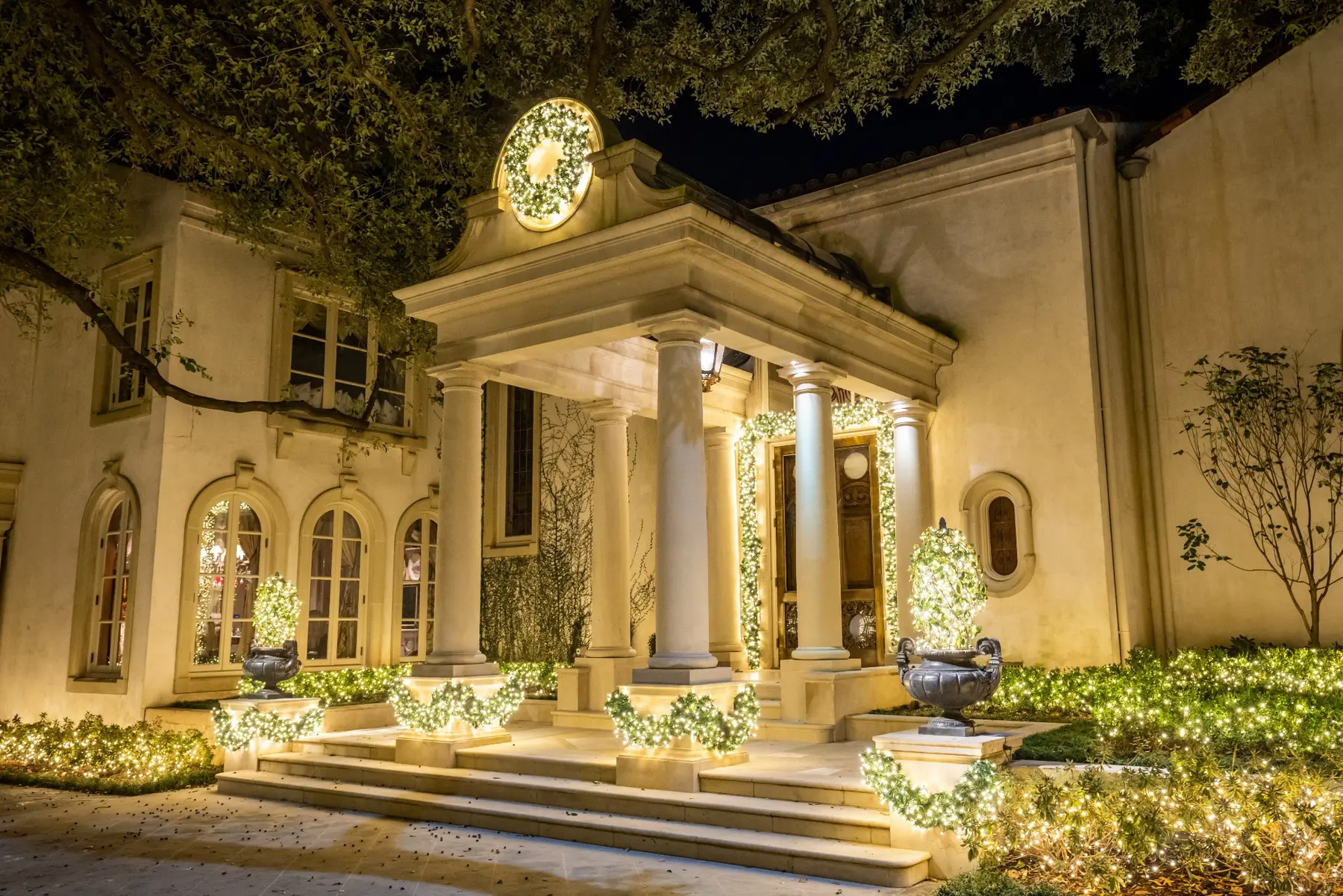 Classical columned home entry with warm white landscape lighting and wreath decor
