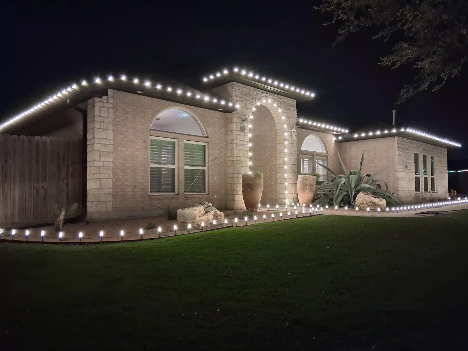 Single-story home with warm white roofline lighting and stake lights tracing the walkway and lawn edge